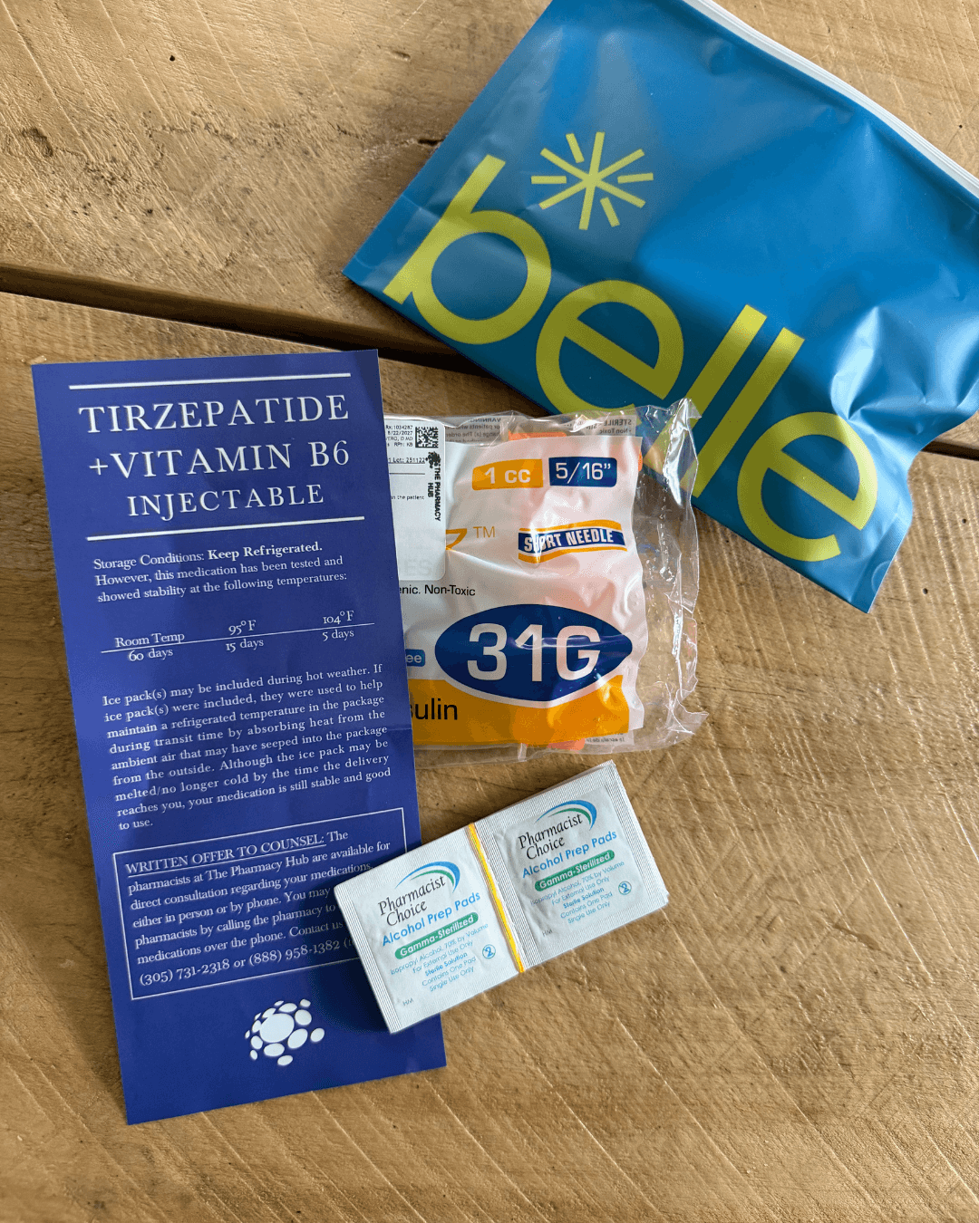 Supplies from a Belle tirzepatide shipment: 1 cc 31G insulin syringes, Pharmacist's Choice alcohol pads, storage card, Belle pouch