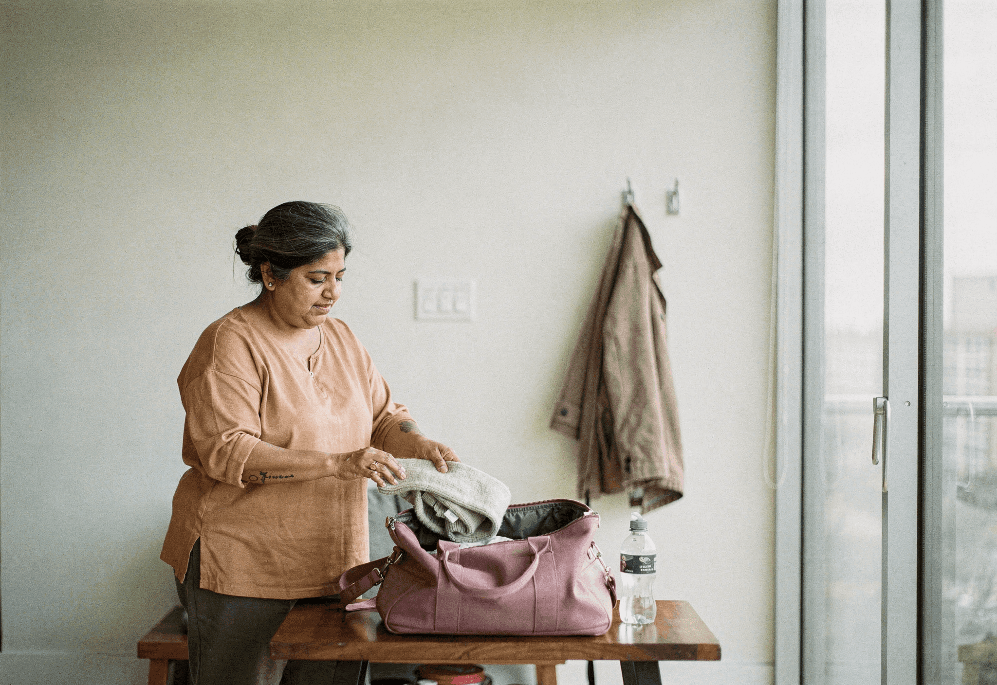 A woman in her late fifties packs a soft purple duffel bag on a bench in a bright room.
