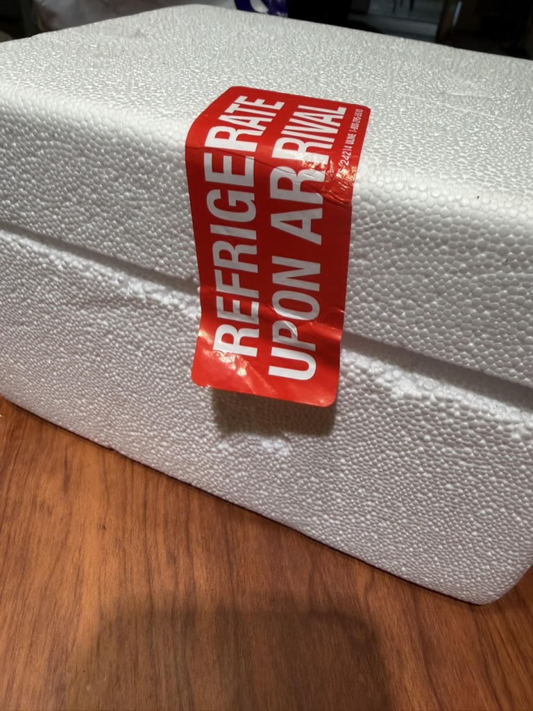 White foam cooler from the Amble shipment sealed with a red REFRIGERATE UPON ARRIVAL sticker across the lid seam