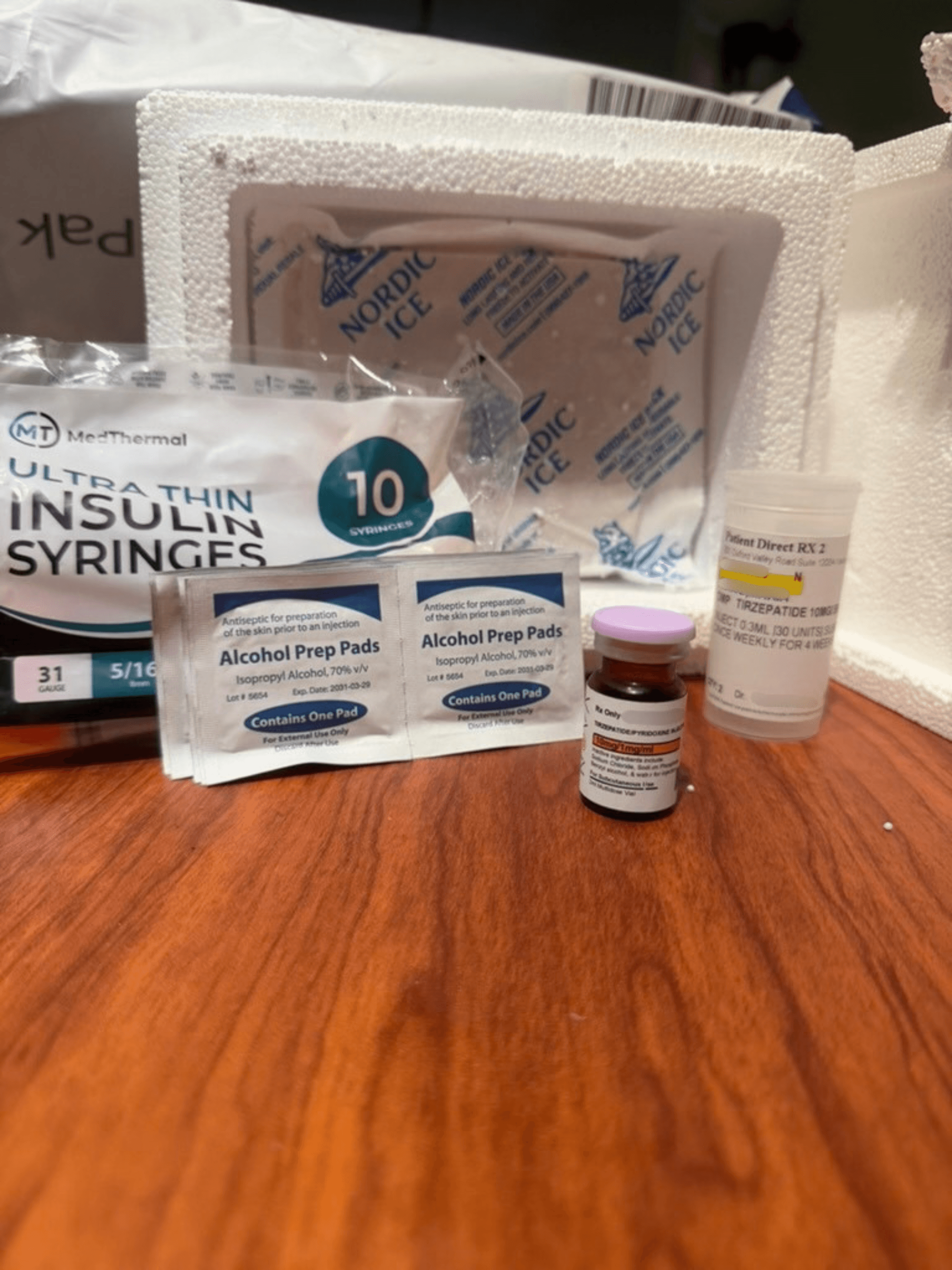 Amble shipment laid out on a table: insulin syringes, alcohol prep pads, an amber tirzepatide vial, a prescription bottle and an ice pack