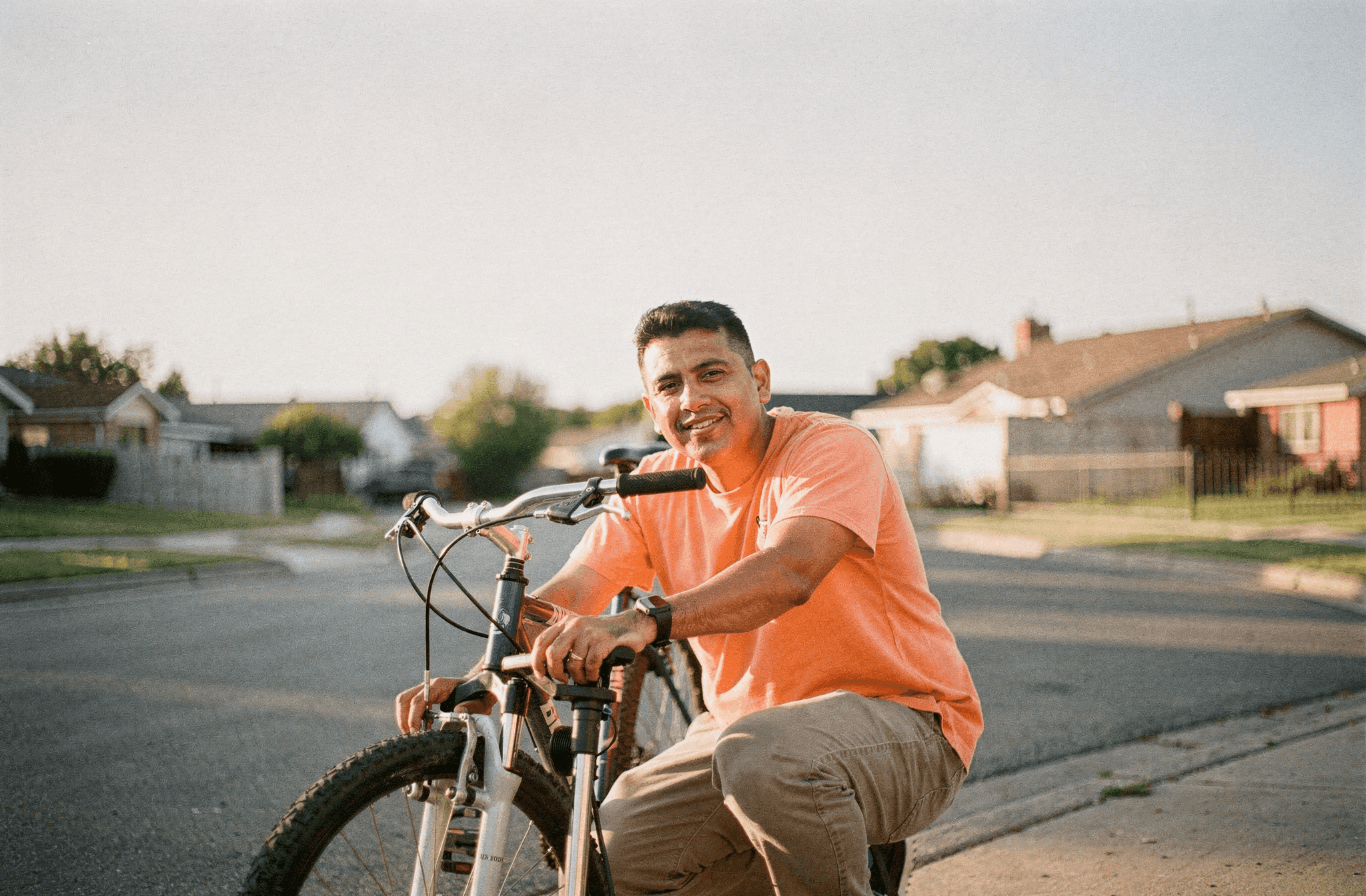 A man in his late thirties crouches beside a bicycle pumping up the front tire on a sunlit street.