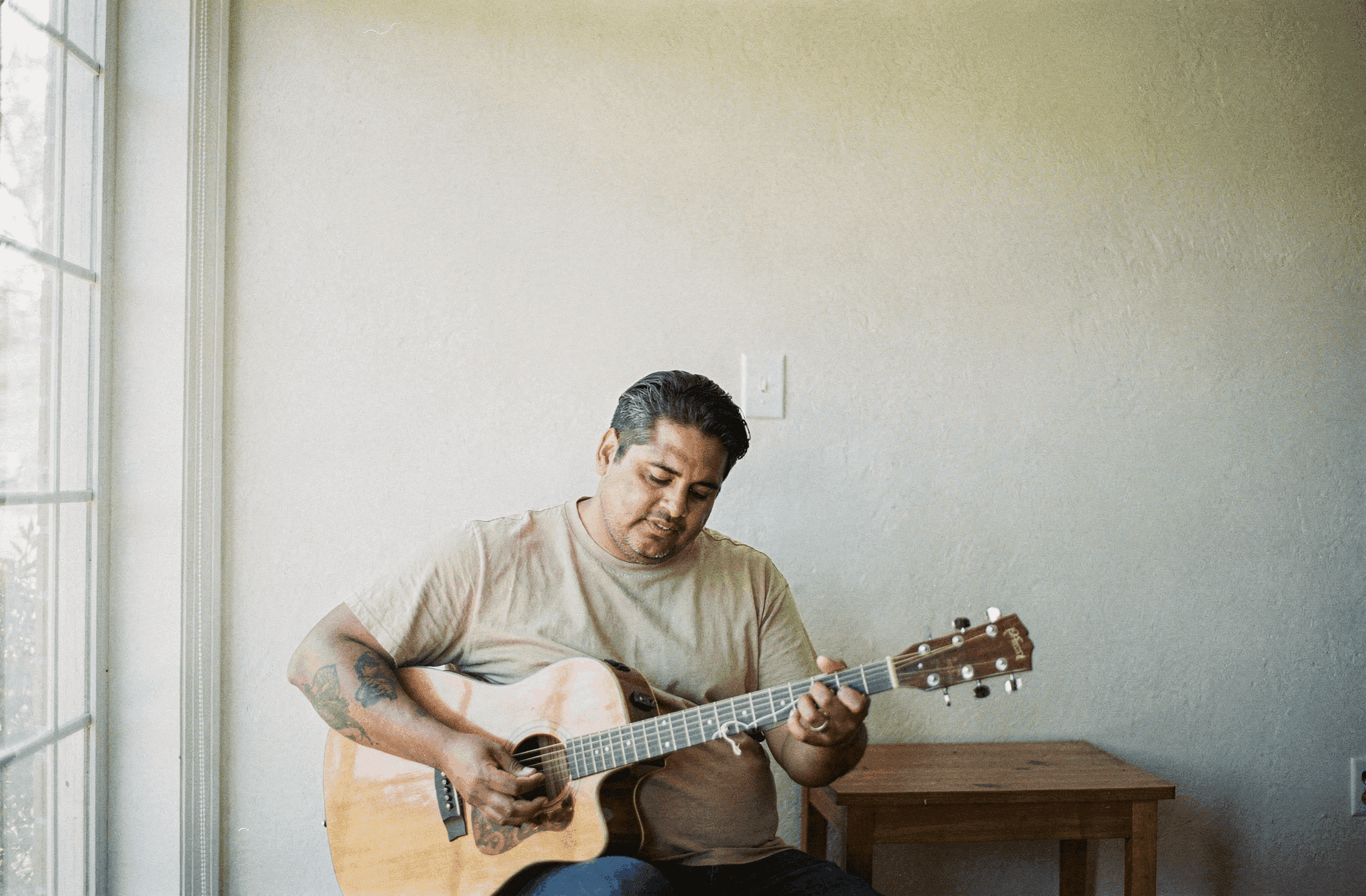 A man in his late forties restrings an acoustic guitar in a bright room.
