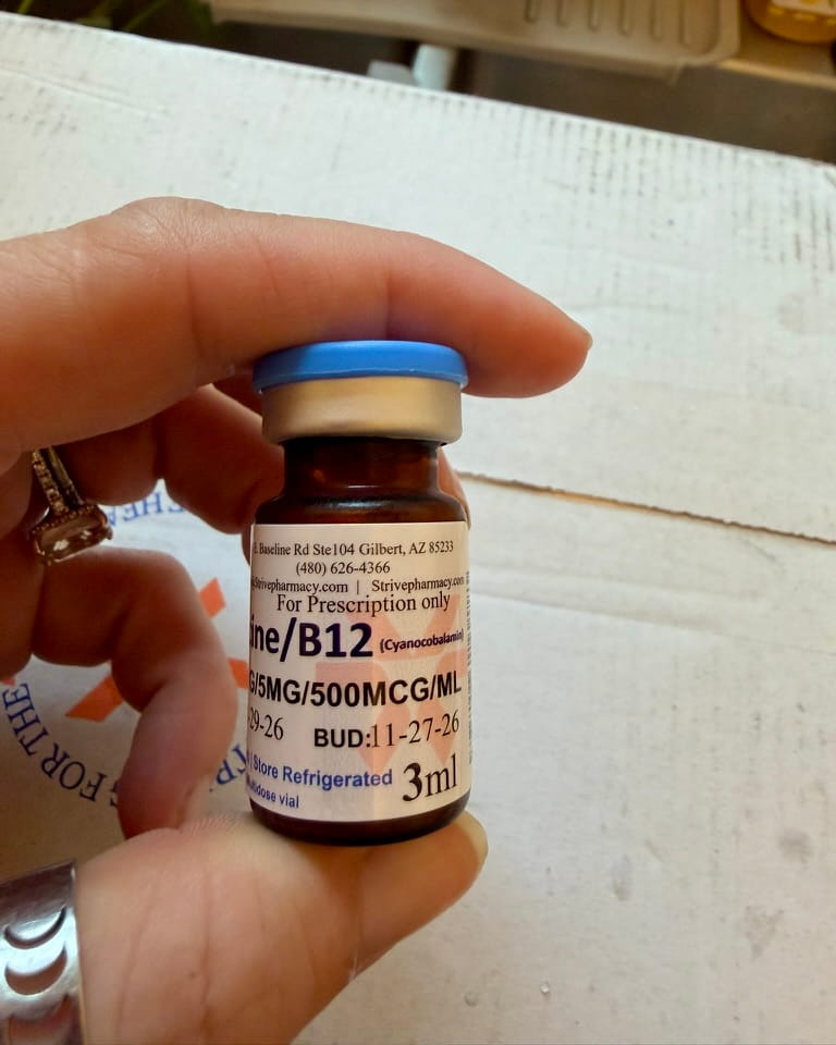 Amber Strive tirzepatide vial with a blue flip cap held in hand, label showing B12 cyanocobalamin, 5 mg and 500 mcg per mL, a BUD of 11-27-26, and 3 ml
