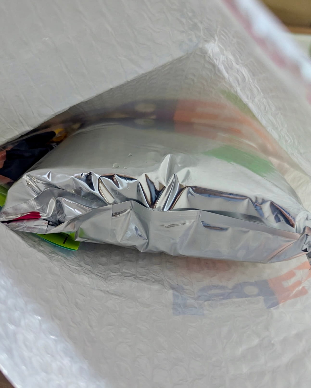 Open FedEx mailer revealing sealed silver mylar pouch with refrigeration labels and gel ice packs inside for temperature-controlled medication delivery