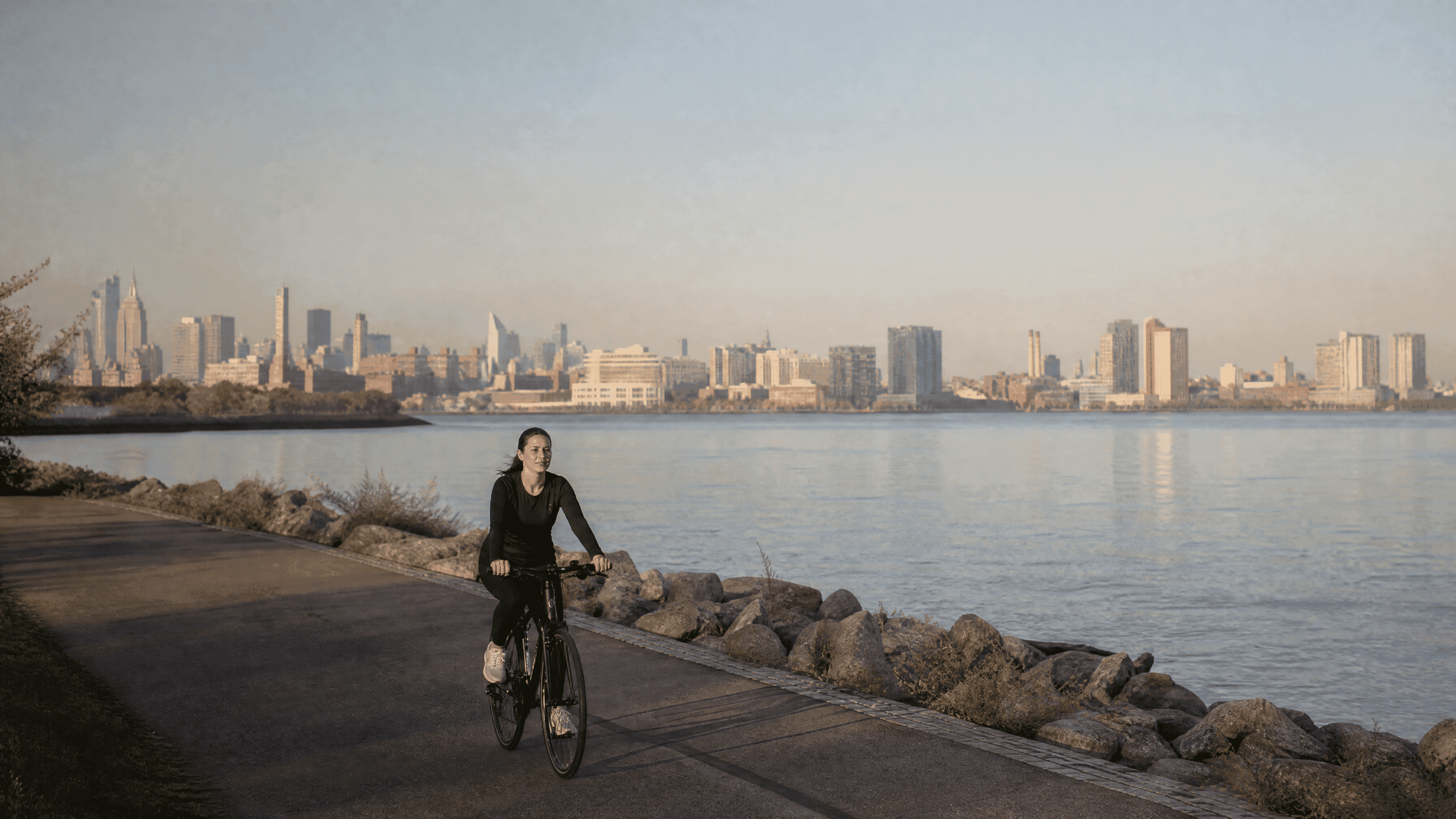 woman in her 30s riding a bicycle on a riverfront path