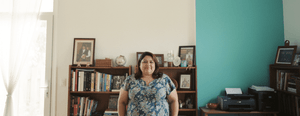 A woman in her late forties lines up an empty picture frame against a wall beside a teal painted panel.